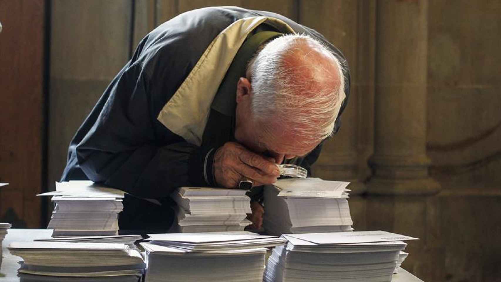 Un hombre observa con una lupa las papeletas de los diferentes partidos.