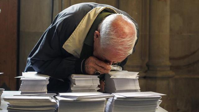 Un hombre observa con una lupa las papeletas de los diferentes partidos.