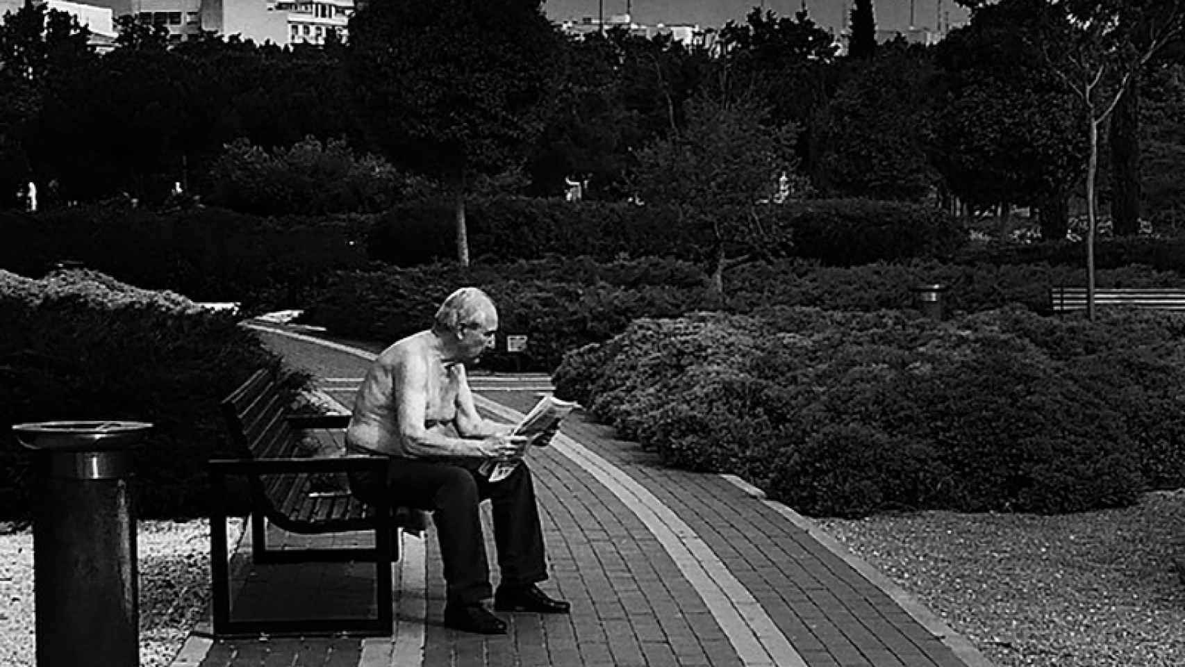 Un hombre lee el periódico en el banco de un parque