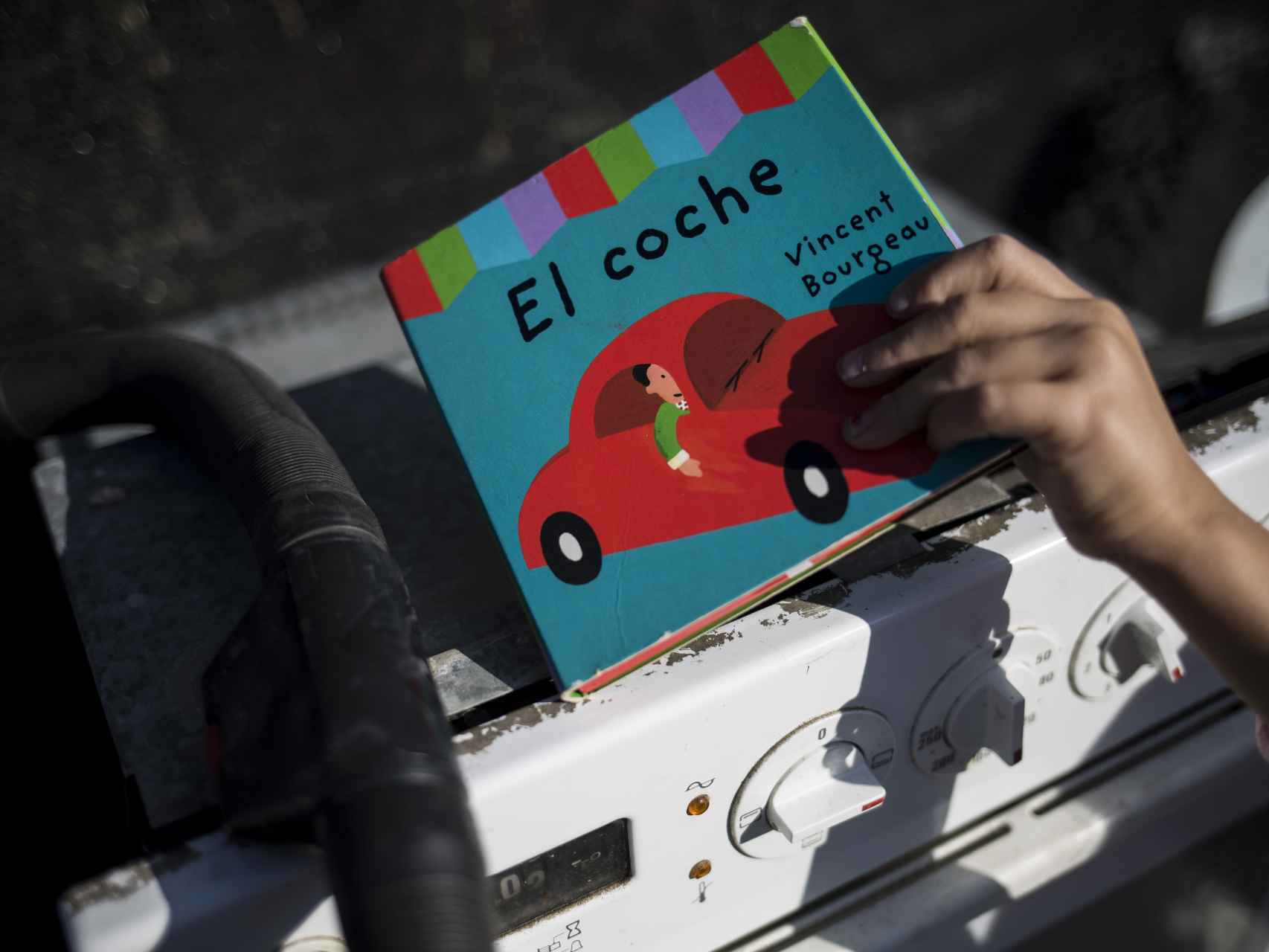 Un niño coge un libro que descansaba sobre un horno desvencijado.