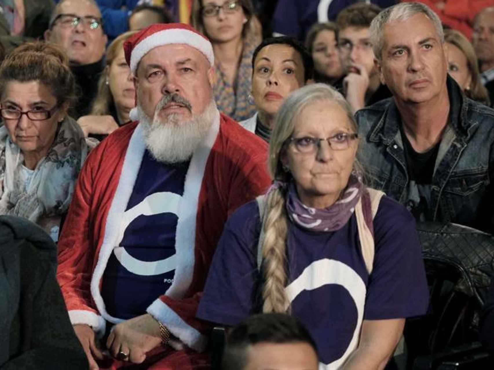 Un asistente disfrazado de Papa Noel atiende al mitin de Podemos.