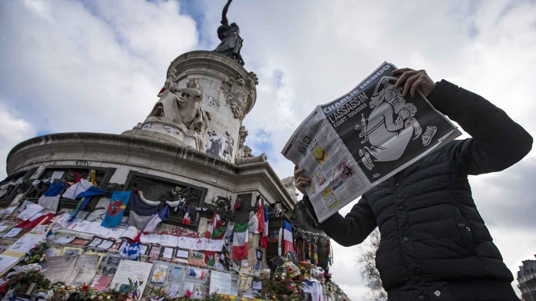Un hombre pasa leyendo 'Charlie Hebdo' ante el homenaje por el aniversario de la tragedia.
