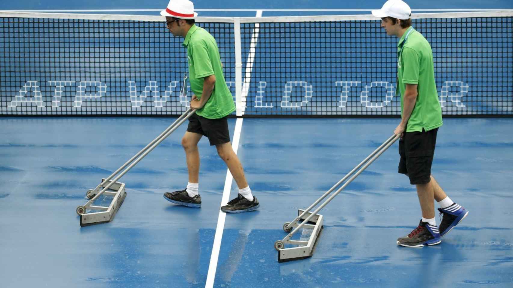 Unos empleados achican agua en una pista, en el torneo de tenis de Sidney