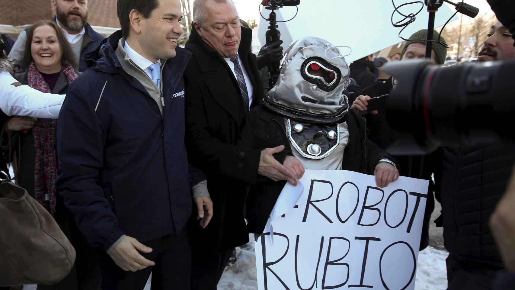 Manifestantes vestidos de robot abordan al candidato Marco Rubio.