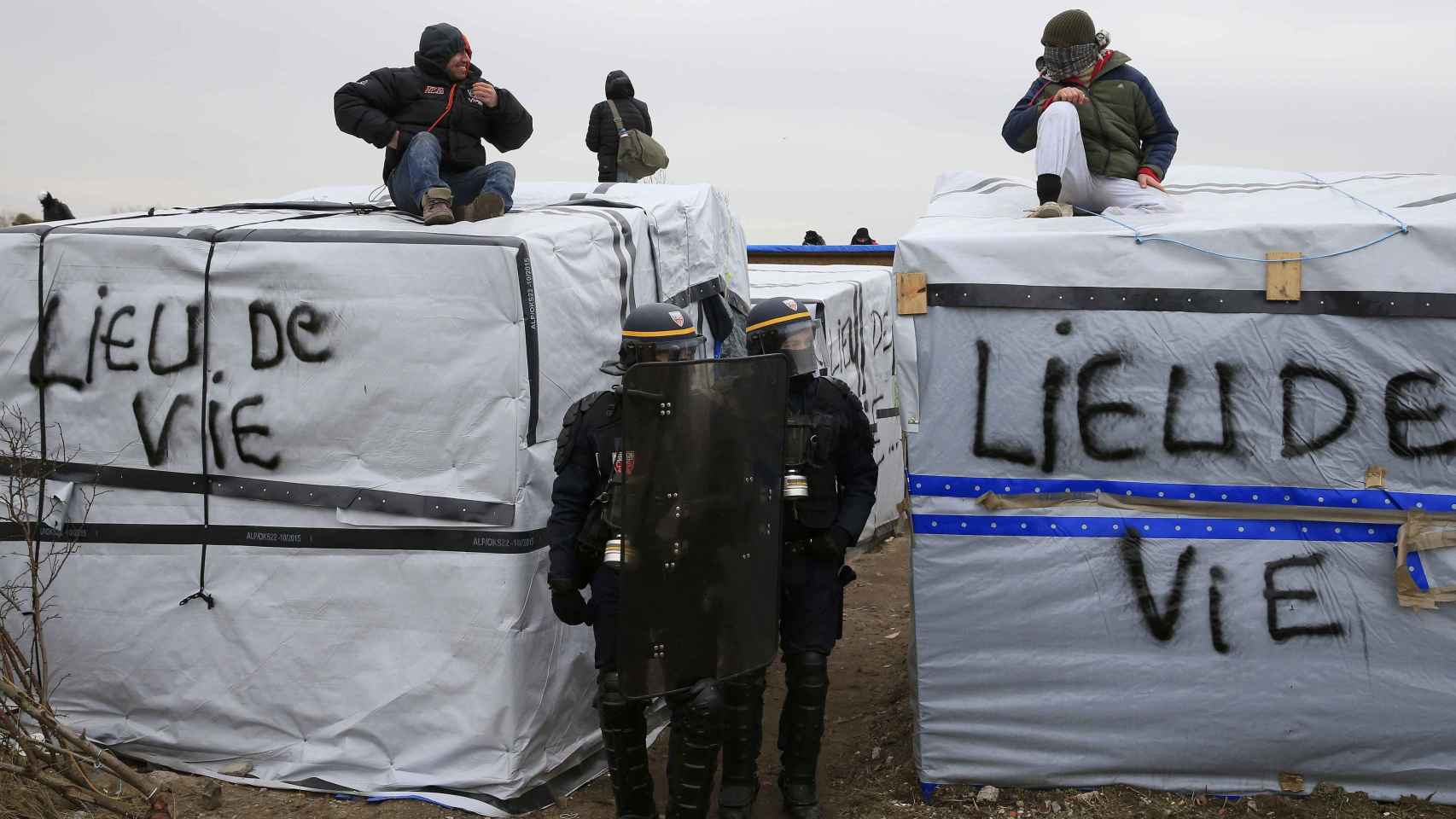 Un grupo de refugiados protesta encima de sus cabañas por el desalojo