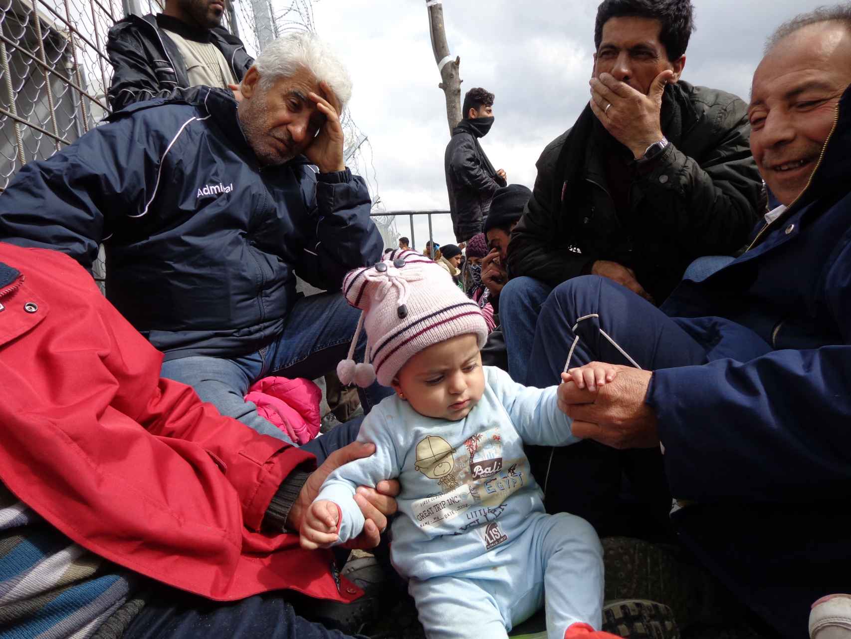 Kur, una bebé siria de 9 meses, espera junto a sus padres al lado de la valla.