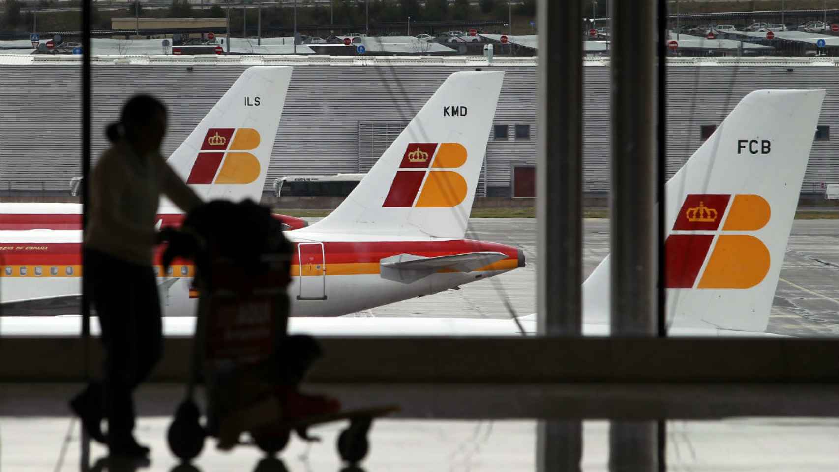 Un pasajero lleva su equipaje ante una hilera de aviones de Iberia.
