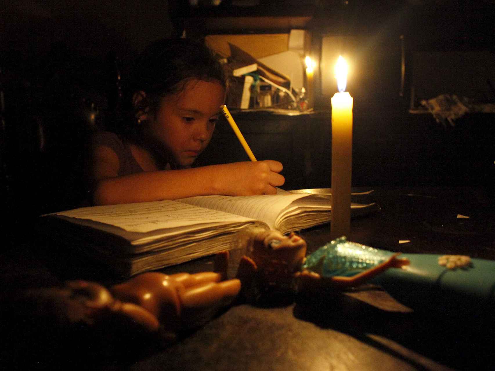 Los cortes de electricidad obligan a esta niña a hacer los deberes con una vela.