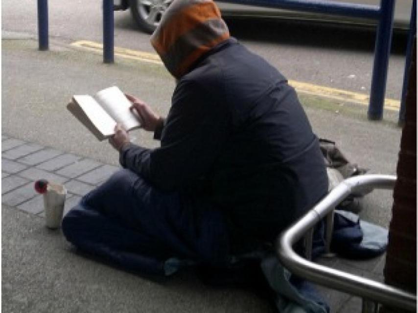 Una persona sintecho leyendo en la calle.