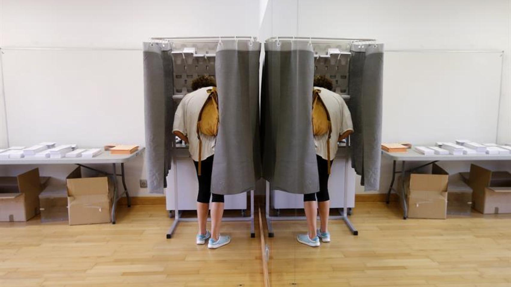 Un elector con su imagen reflejada en un espejo elige su papeleta para ejercer su derecho al voto en el Centro Cultural Volturno, en la localidad madrileña de Pozuelo de Alarcón.