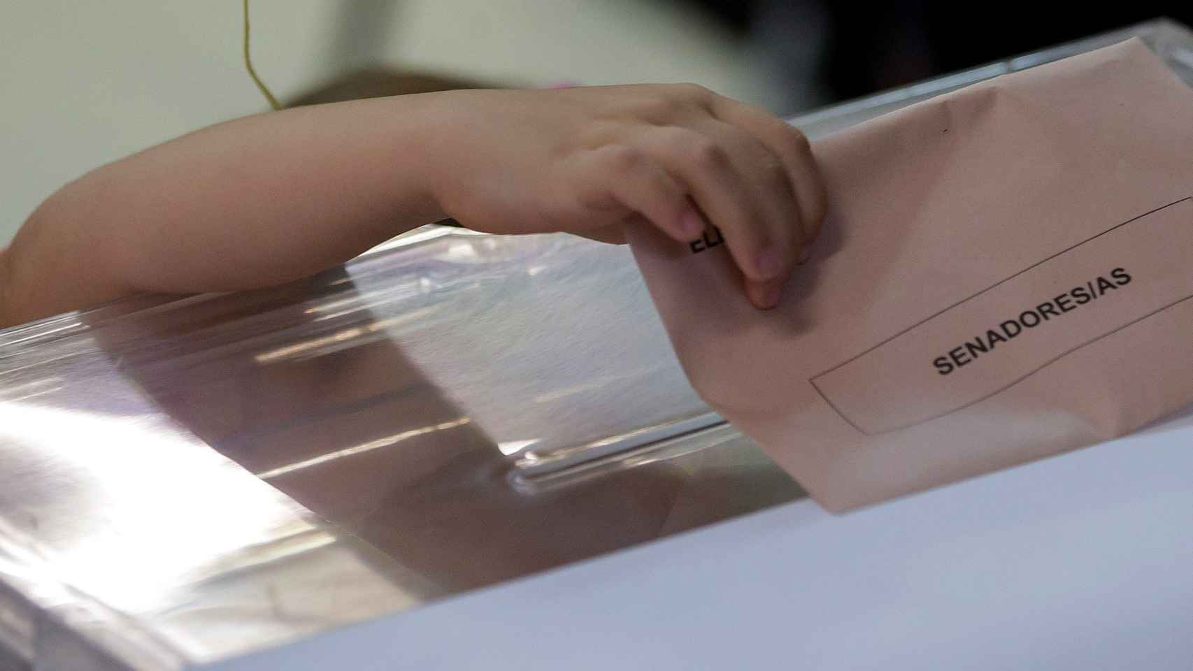 Una niña intenta meter el sobre en la urna con el voto de su madre, en Sevilla.