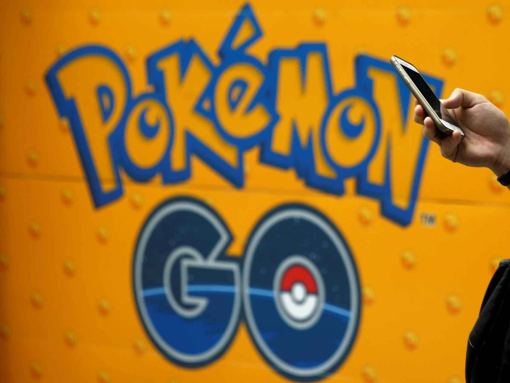 Un hombre usa su móvil frente a un cartel de Pokémon Go en Tokyo.