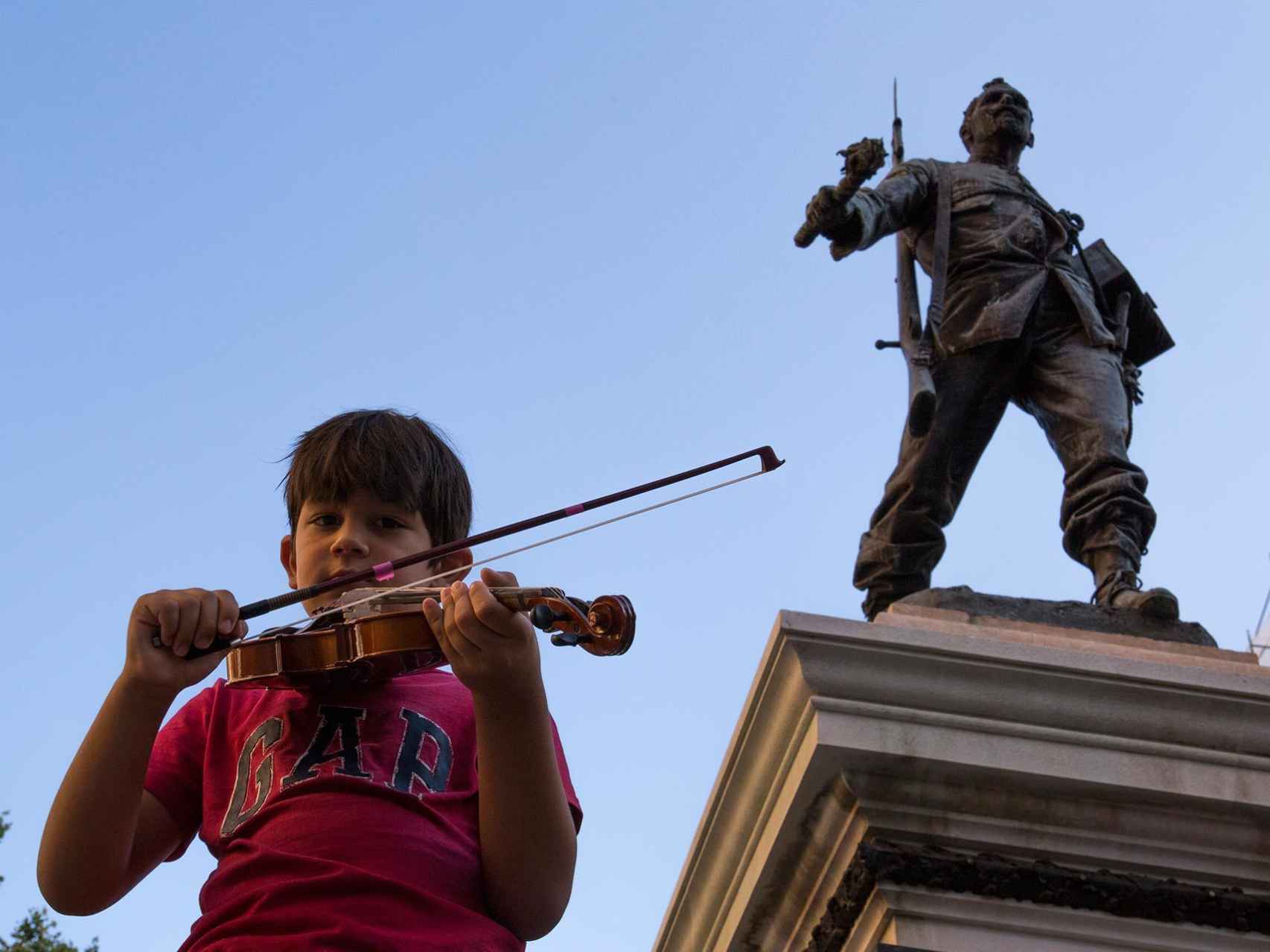 Un joven violinista junto a la estatua de Eloy Gonzalo, en la Plaza de Cascorro, epicentro de las fiestas de San Cayetano.