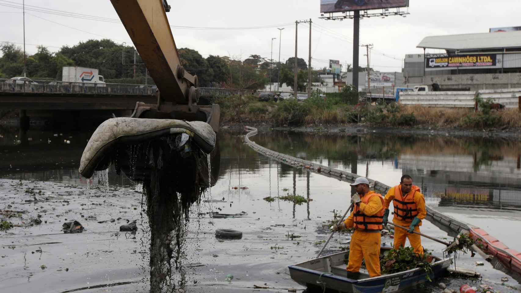 Unos operarios limpian basura cerca de una ecobarrera en un río que da a la bahía de Guanabara.