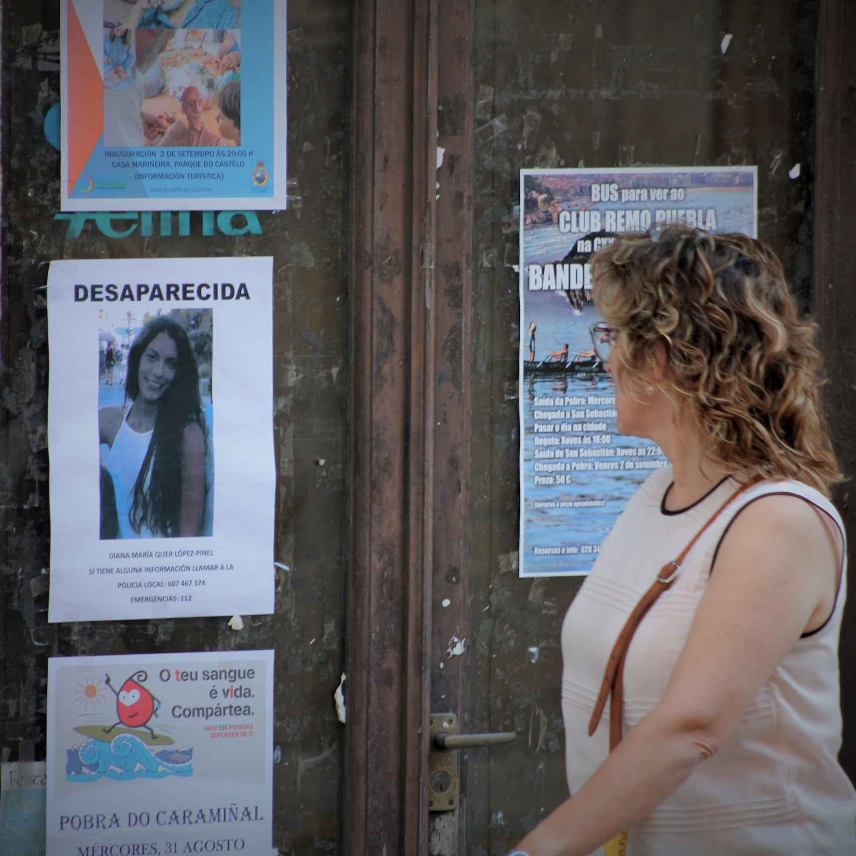 Una mujer pasa junto a un cartel donde se pide información sobre Diana Quer.