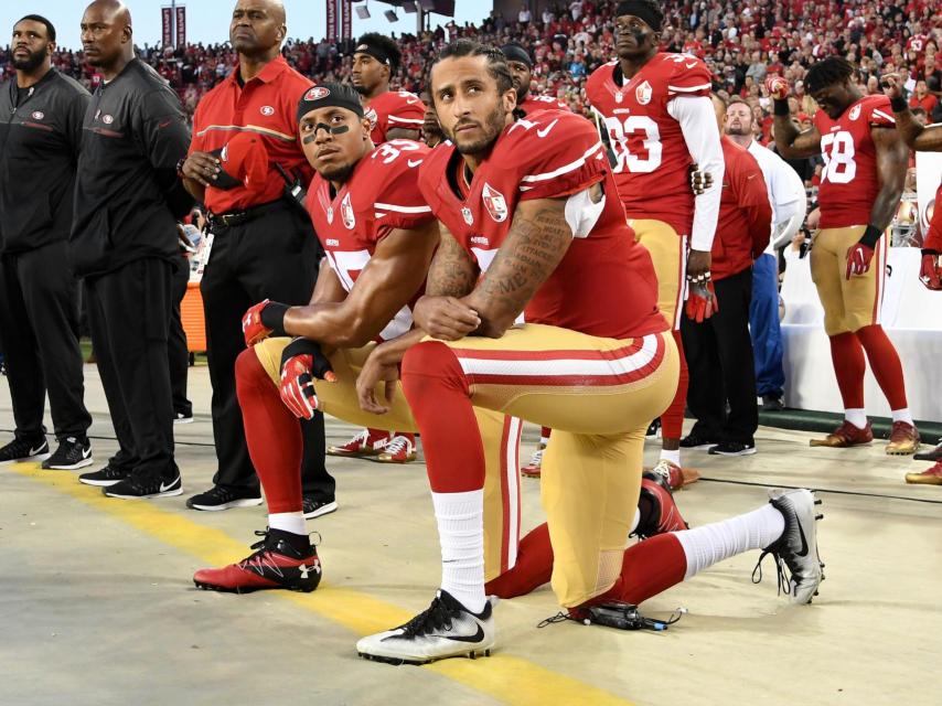 Kaepernick, en primer plano, rodilla en tierra durante el himno.