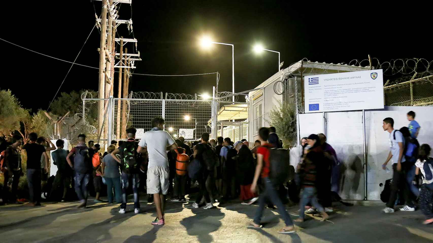 Refugiados y migrantes esperan junto a una puerta cerrada del campo de Moria tras el incendio.