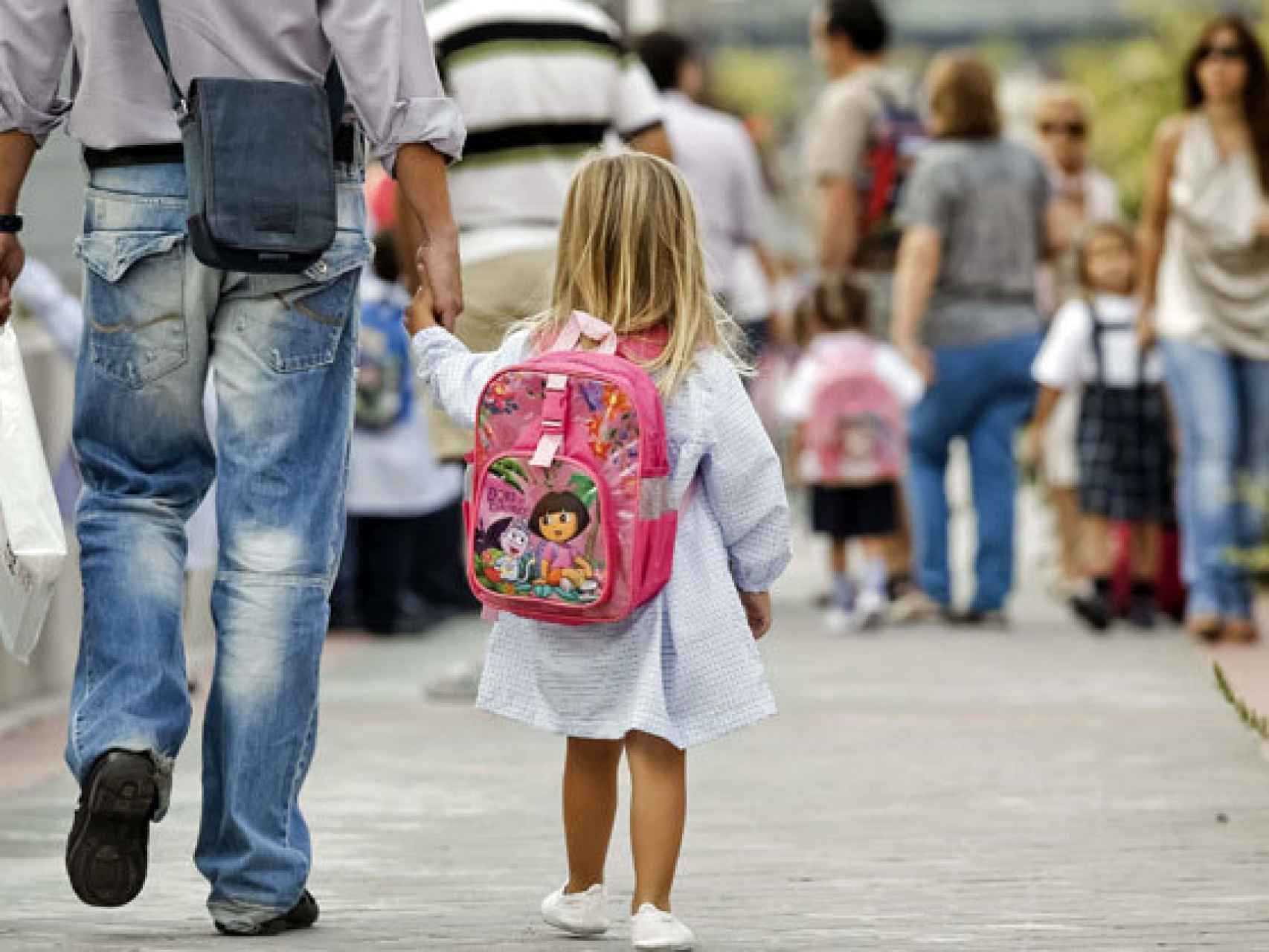 Una niña camina con su padre al colegio.