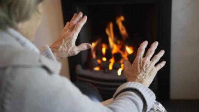 Una anciana se calienta frente a una chimenea.