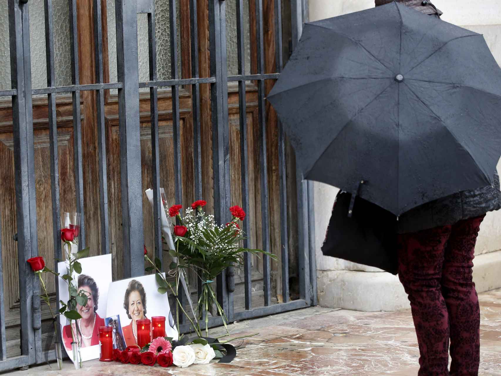 Una persona se para ante unas fotografías y flores colocadas por personas anónimas en uno de las puertas del Ayuntamiento de Valencia en memoria de Rita Barberá.