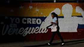 Una mujer camina ante un mural de una calle de Caracas.