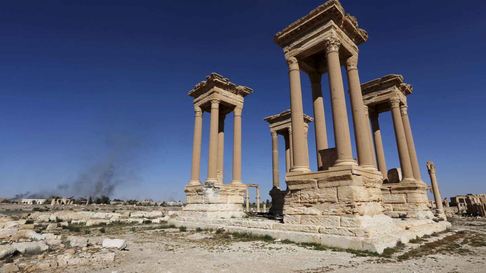 Ruinas de la ciudad histórica de Palmira, con humo al fondo en la ciudad moderna.