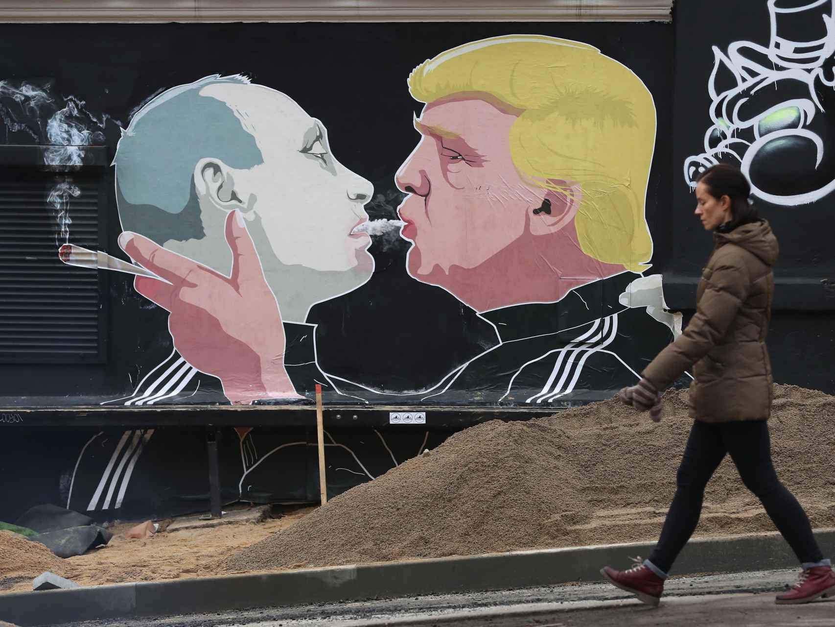 Una mujer recorre un mural en Vilnius, Lituania, que muestra a Trump fumando marihuana en la boca junto a Vladimir Putin.