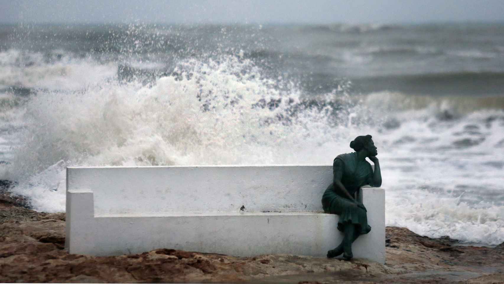 - Las olas rompen contra las rocas tras la escultura de la bella Lola, en el paseo marítimo de Torrevieja (Alicante).