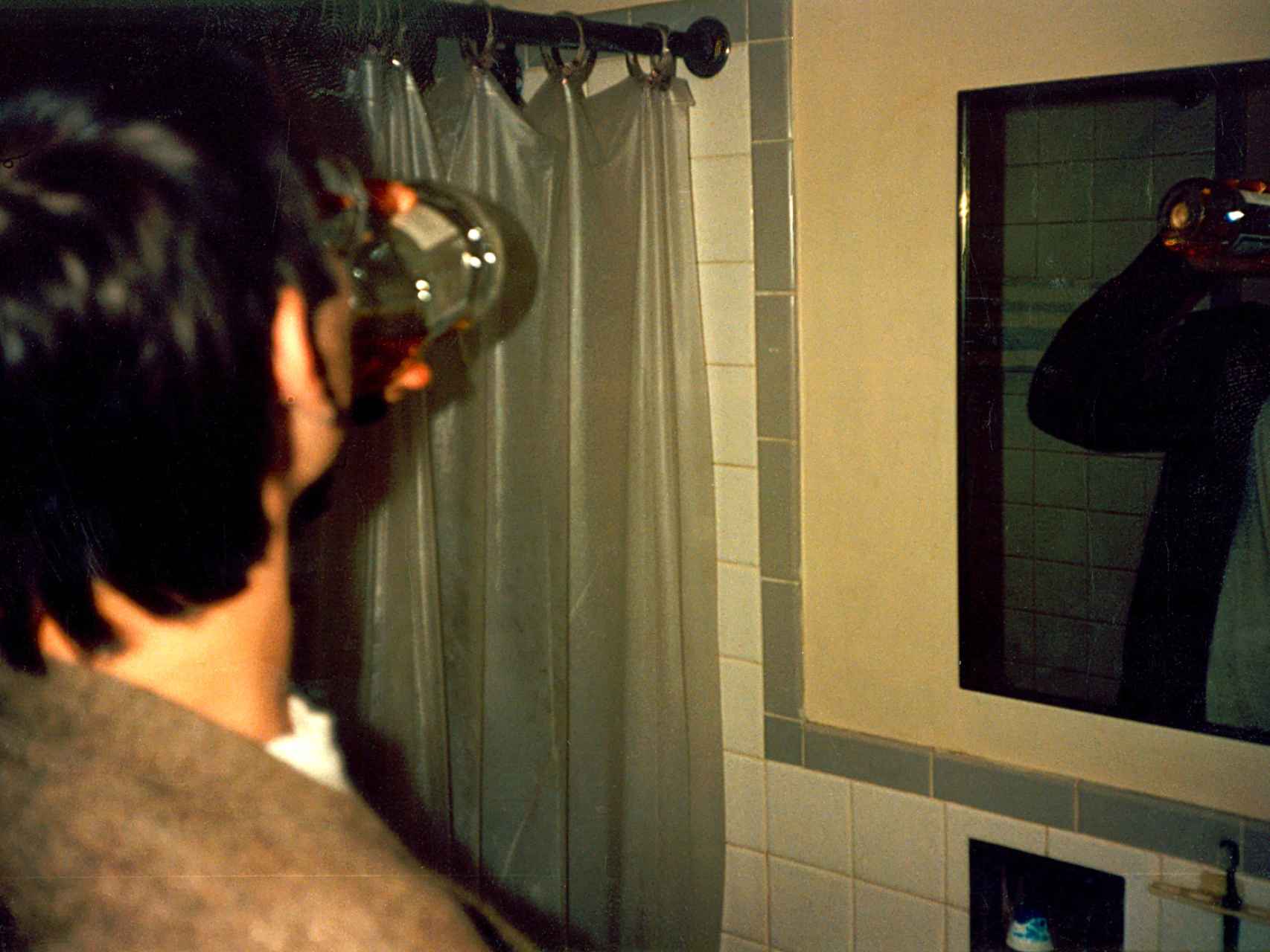 Un joven degusta un chupito de colutorio frente al espejo.