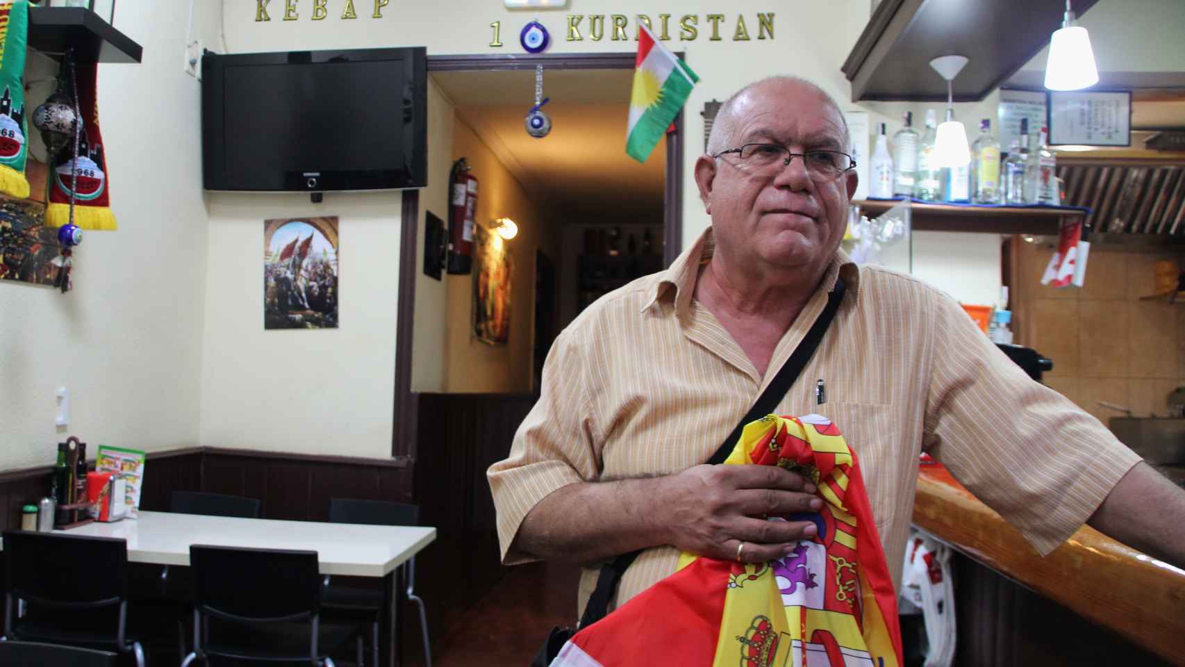 Mahmud Abdi, en un establecimiento de comida rápida de Vallecas, en Madrid, sostiene una bandera española en agradecimiento a su país de acogida.