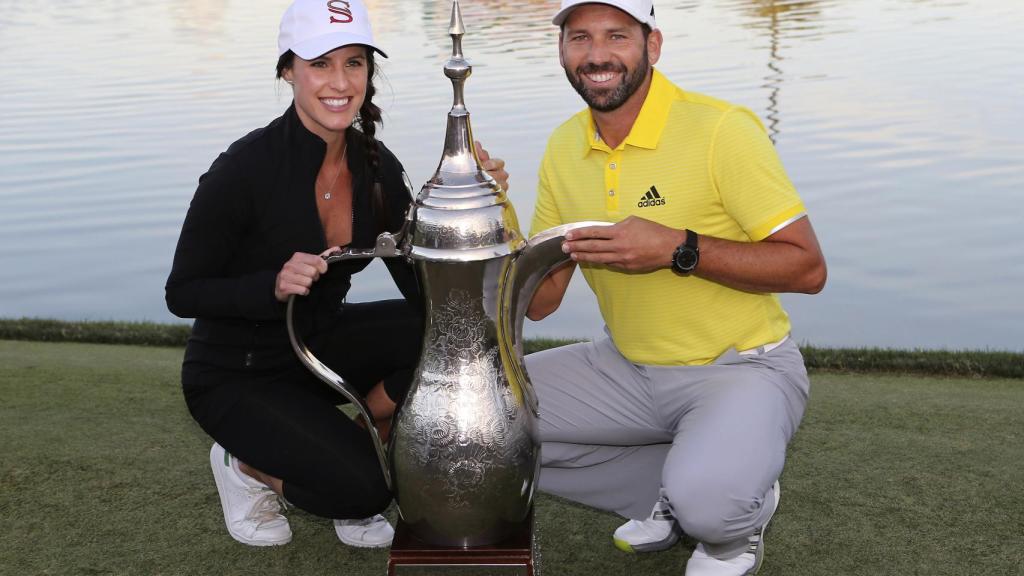 Angela Akins y Sergio García posan sonrientes junto al trofeo del golfista en Dubai.