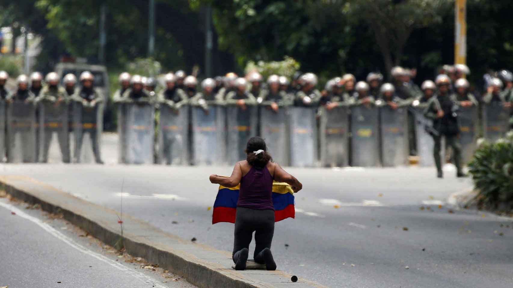 Una manifestante, de rodillas frente  al cordón policial en Caracas