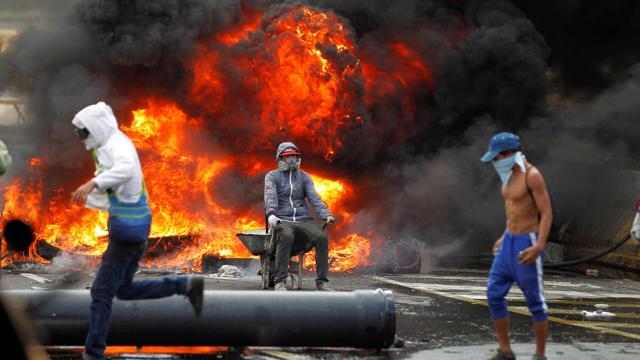 Tres manifestantes construyen una barricada en plena calle en Caracas.