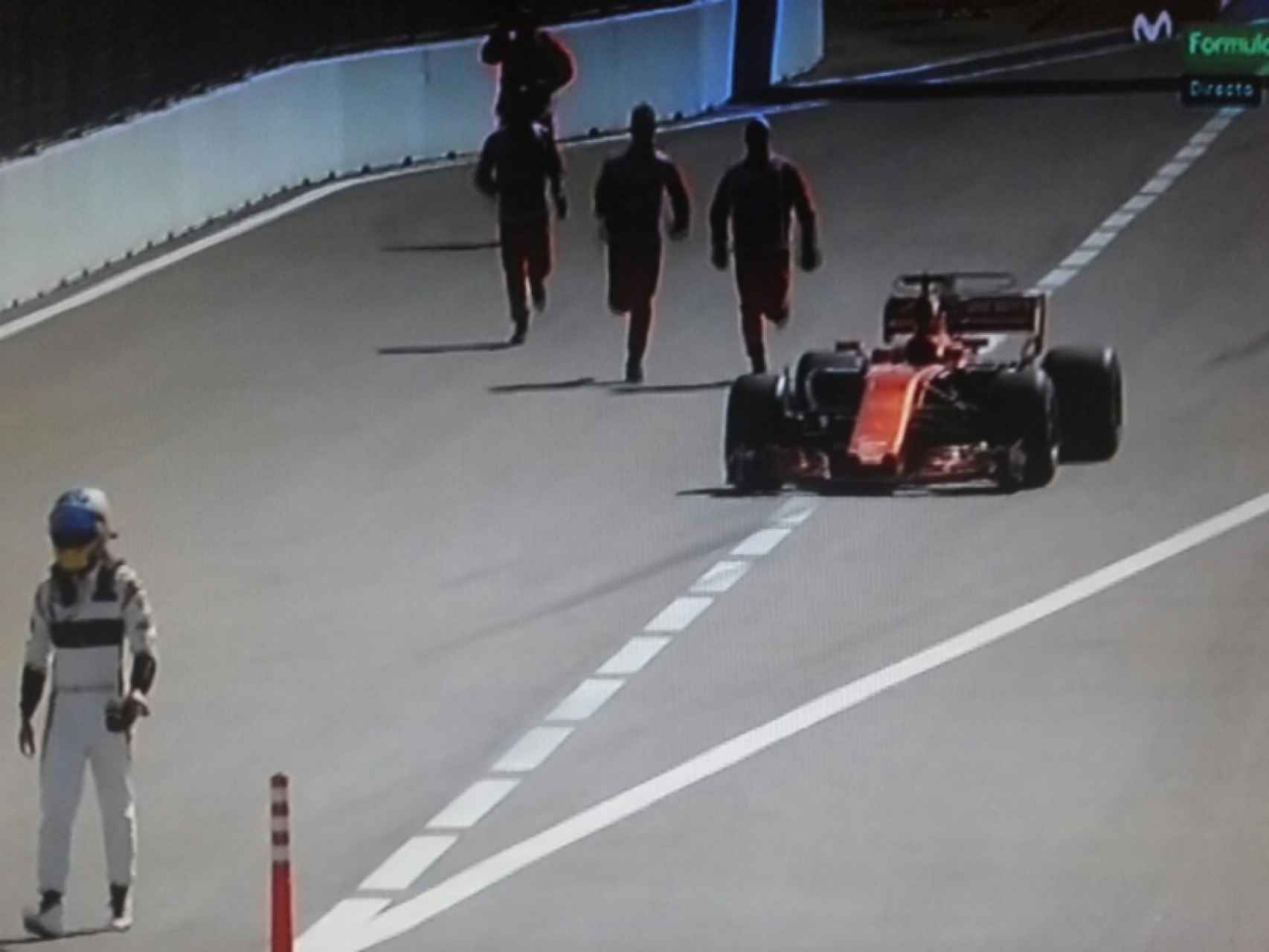 Alonso camina con su McLaren parado en la entrada de boxes.