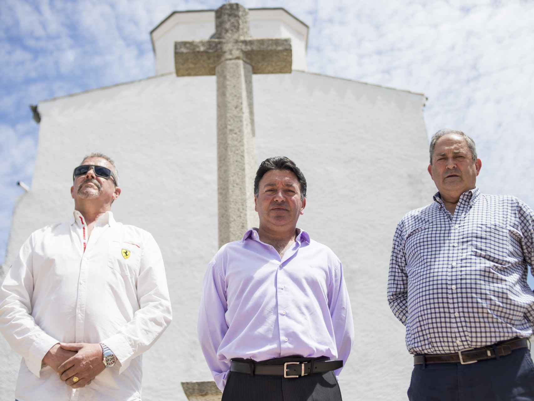 El alcalde (centro) con dos vecinos del pueblo frente a la cruz que emula a la del Valle de los Caídos y frente a la  cual pretenden enterrar al dictador.