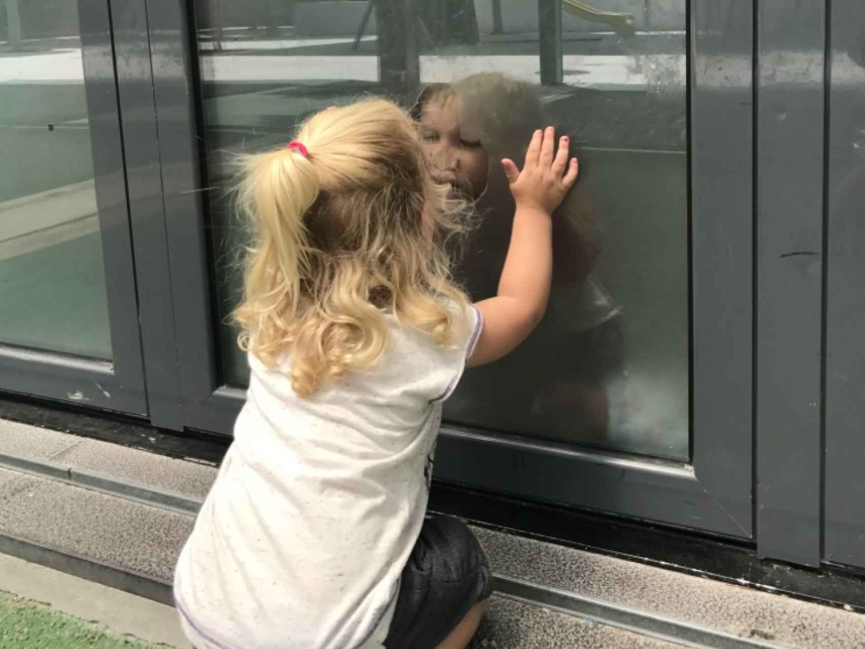 Malin, de dos años, mira por un cristal de su colegio a su hermano mayor.