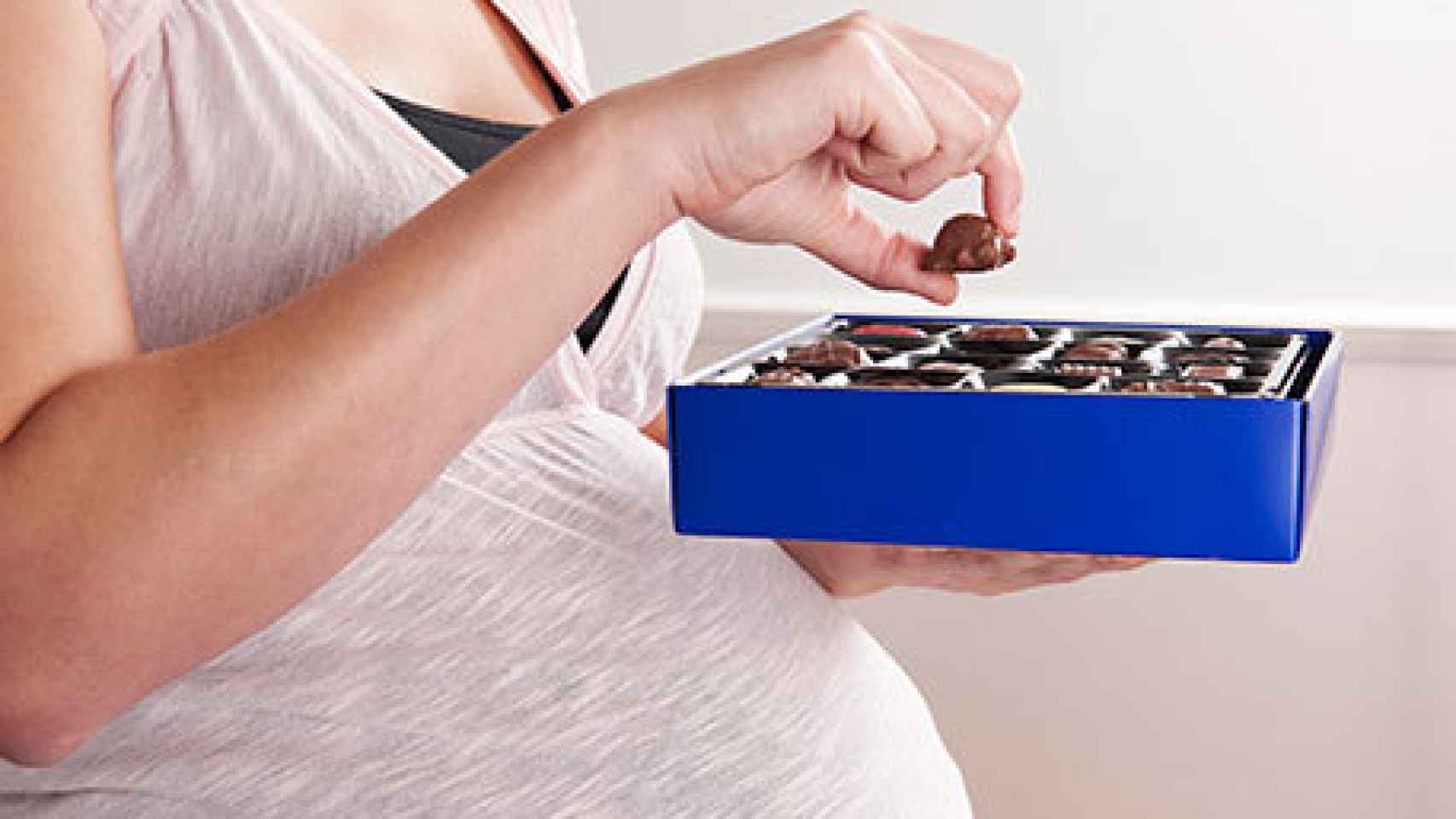 Una mujer embarazada sostiene una caja de bombones.