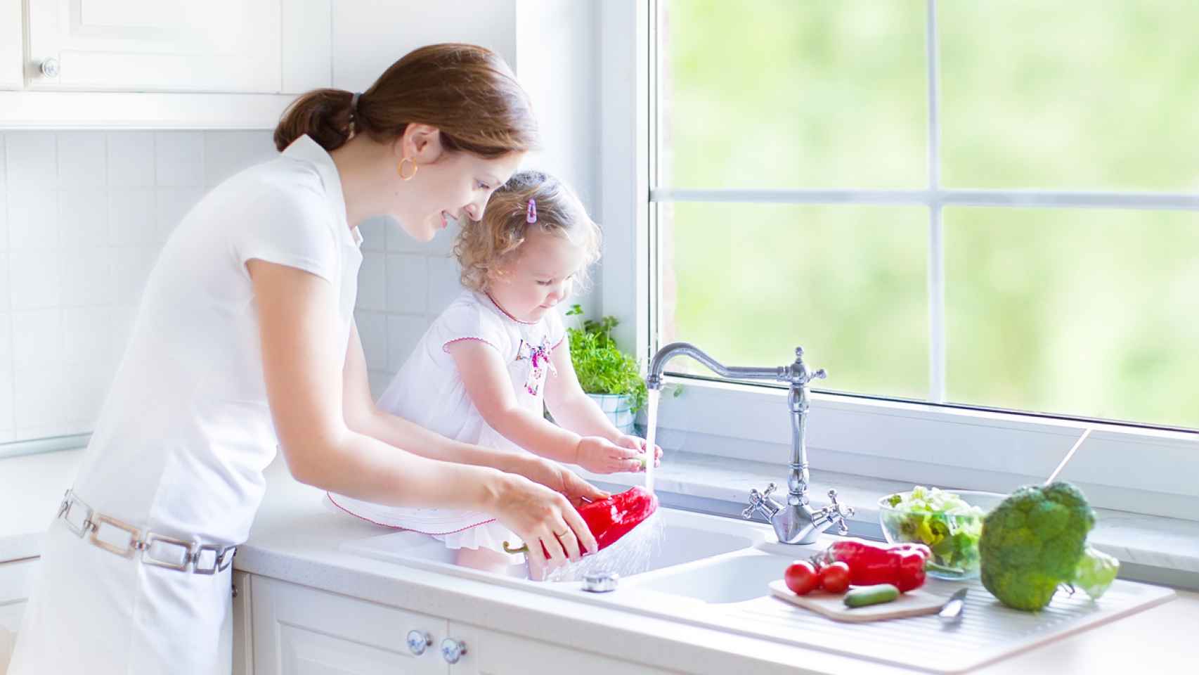 Beautiful mother and her daughter washing vegetables in kitchen sink