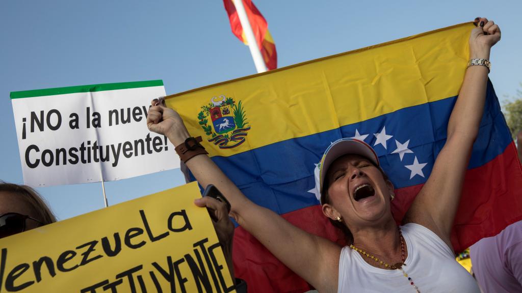 Una mujer sostiene una bandera de Venezuela entre pancartas contrarias a la Constituyente en Madrid.