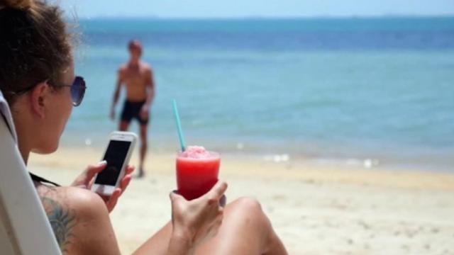 Una chica consulta su móvil en la playa.