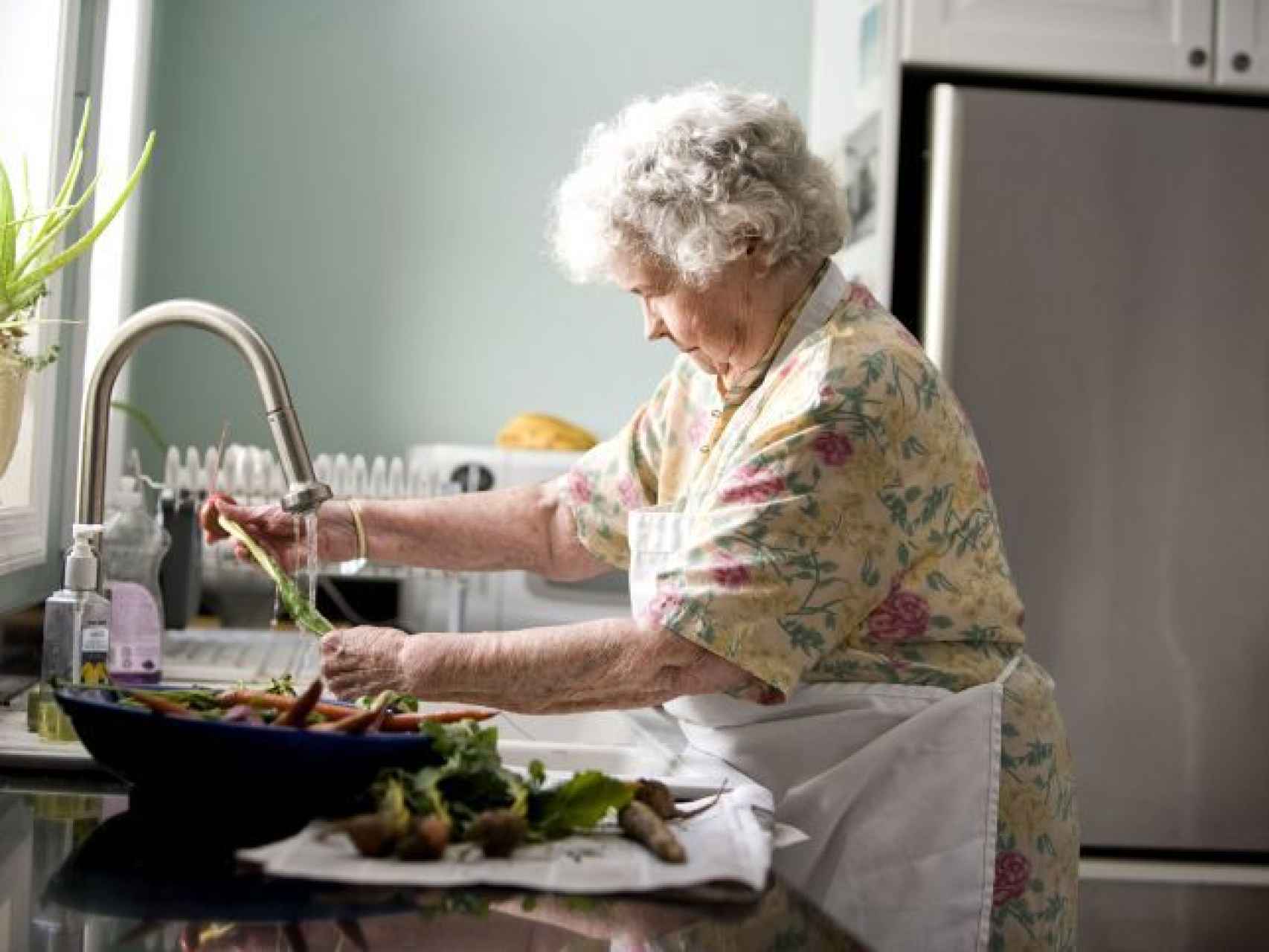 Una anciana lava verduras con agua.