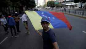 Un opositor enarbola una bandera venezolana en una avenida desierta