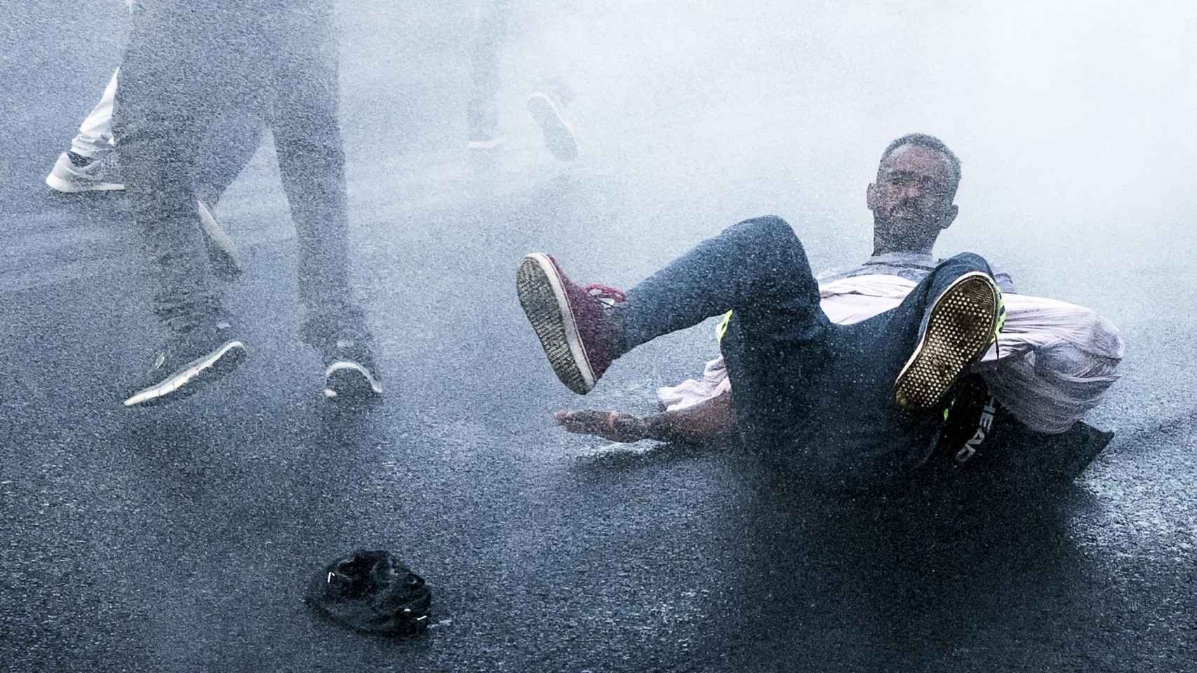 Un inmigrante, en el suelo tras ser aturdido por un cañón de agua.
