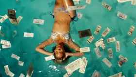Una mujer se baña en una piscina bajo una lluvia de billetes.