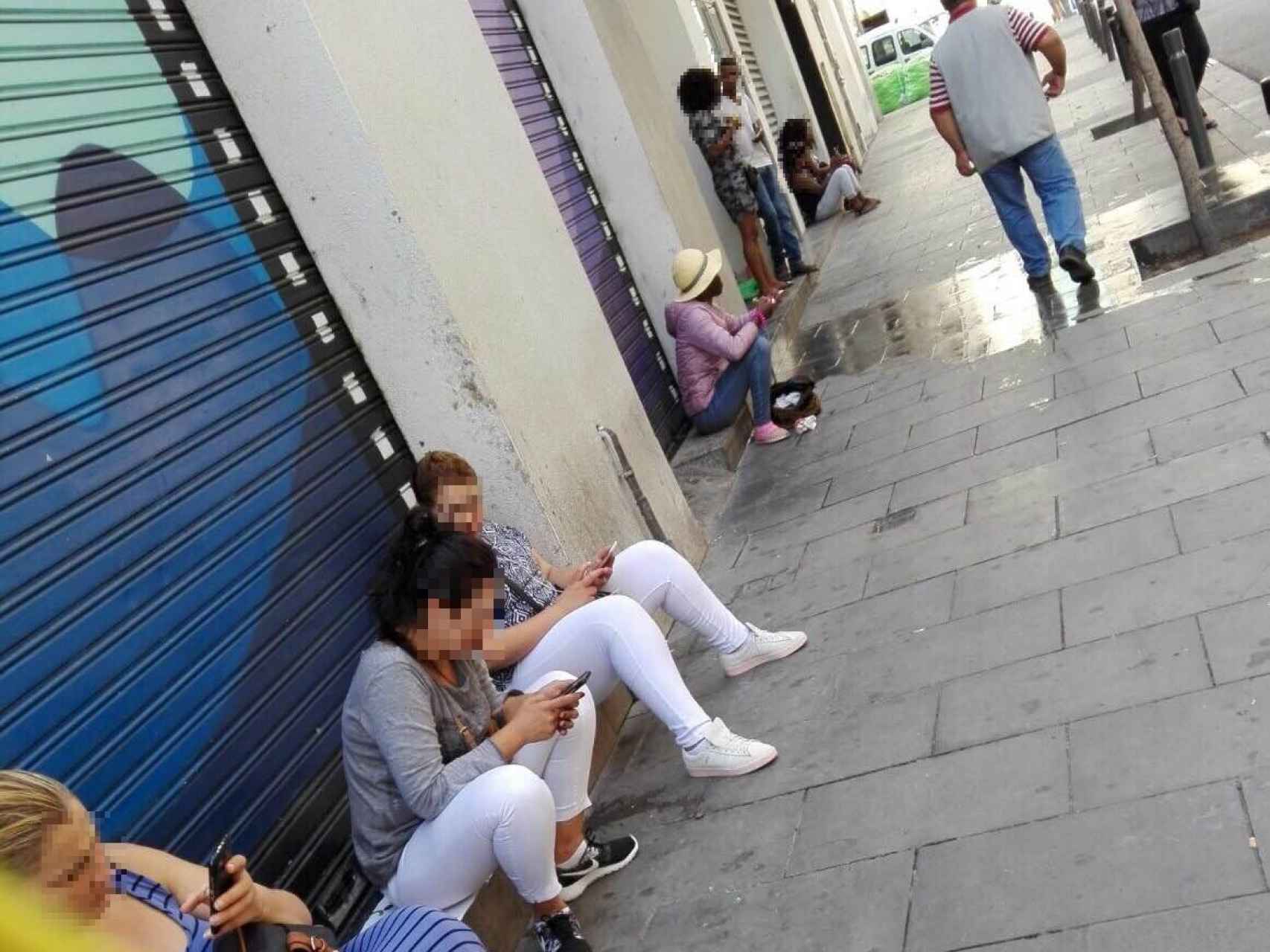 Algunas mujeres esperan a sus clientes sentadas en los escalones de los locales de la calle
