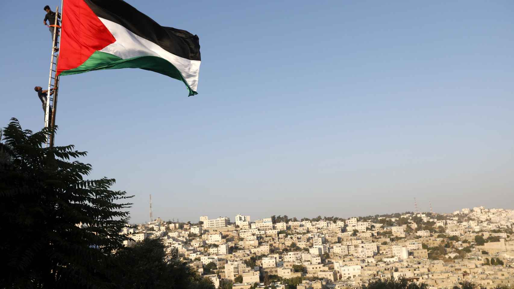 Unos manifestantes palestinos izan una bandera en Hebrón.