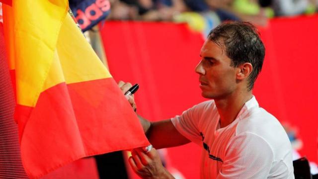 Nadal firma un autógrafo sobre una bandera de España.