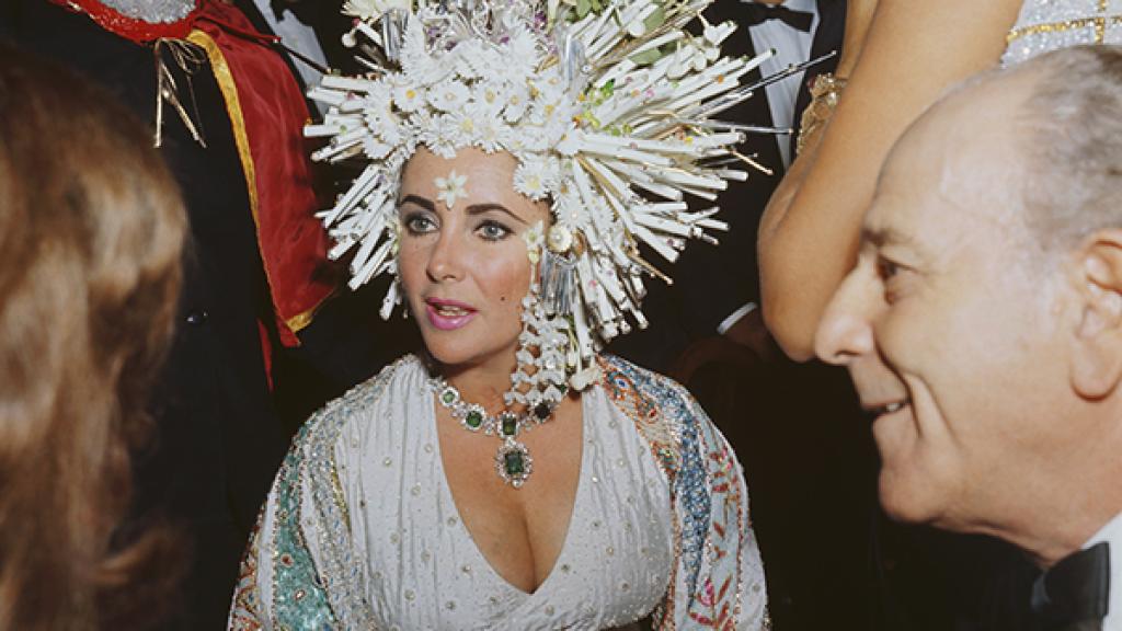 En una gala benéfica con un tocado de perlas y flores artificiales, un vestido joya y collar de esmeraldas, haciendo alarde de su particular estilo “más es más”.