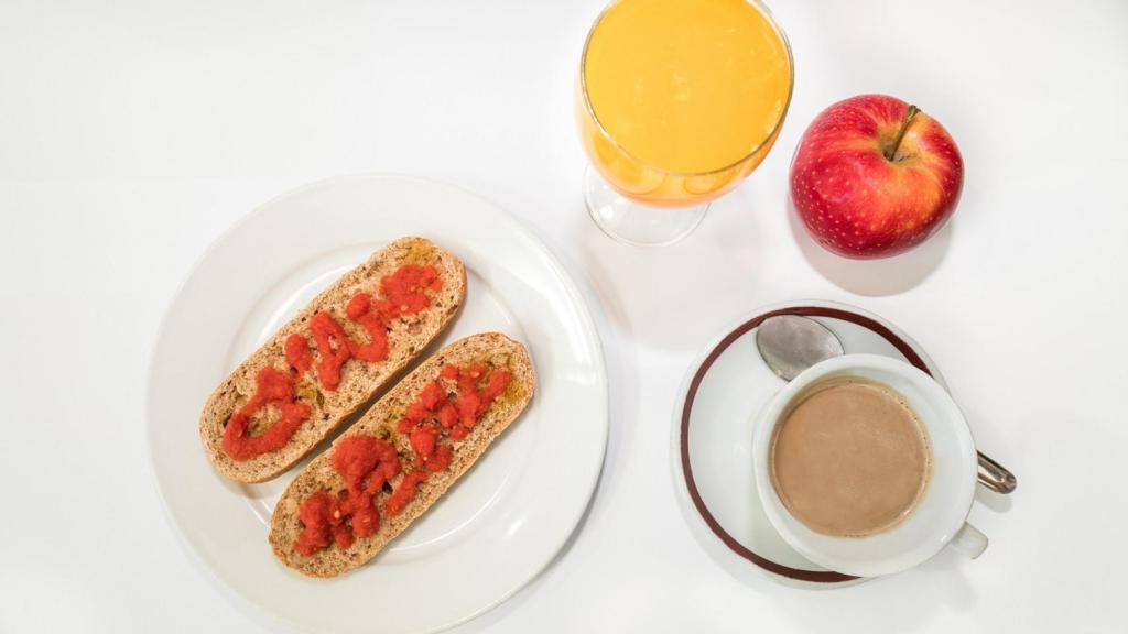 Una taza de café con leche, fruta y pan integral con tomate y aceite de oliva.