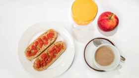 Una taza de café con leche, fruta y pan integral con tomate y aceite de oliva.